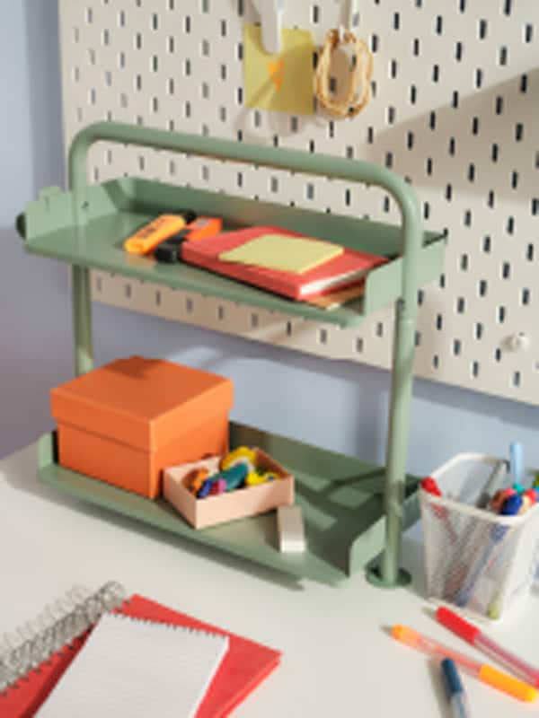 A light grey-green RELATERA desktop shelf on a white desk with stationery on it, and a white SKÅDIS pegboard behind it.