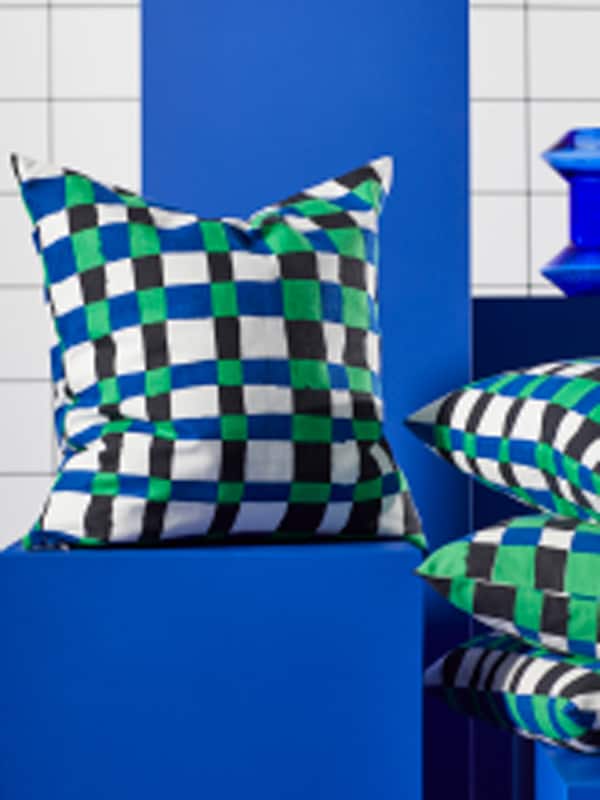 A PLATTLUMMER cushion on a blue podium, next to it is a couple of other PLATTLUMMER cusions stacked on top of each other.