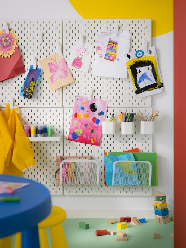 Children’s artwork hang on four SKÅDIS pegboards. A SKÅDIS shelf, containers, and magazine holders keep art supplies tidy.