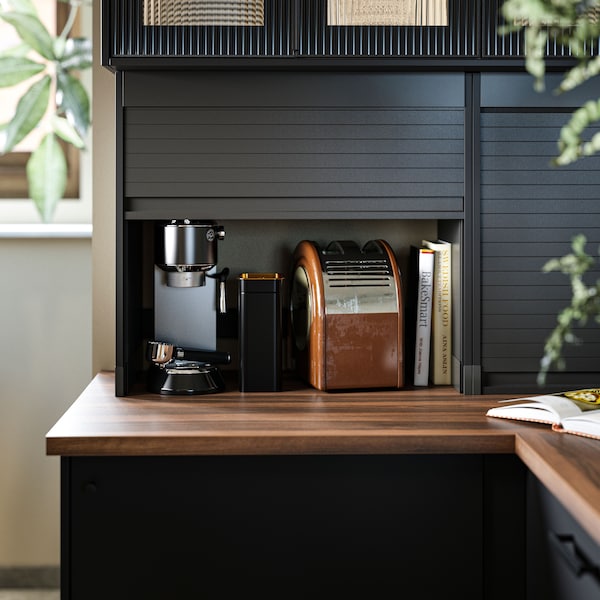 A kitchen with EKBACKEN worktop in brown walnut effect/laminate, with TITTEBO tambour storage, kitchen appliances and books.