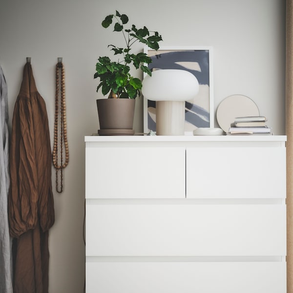 A MALM chest of drawers with three large drawers and two small. A plant, a table lamp and vases are displayed on top of it.