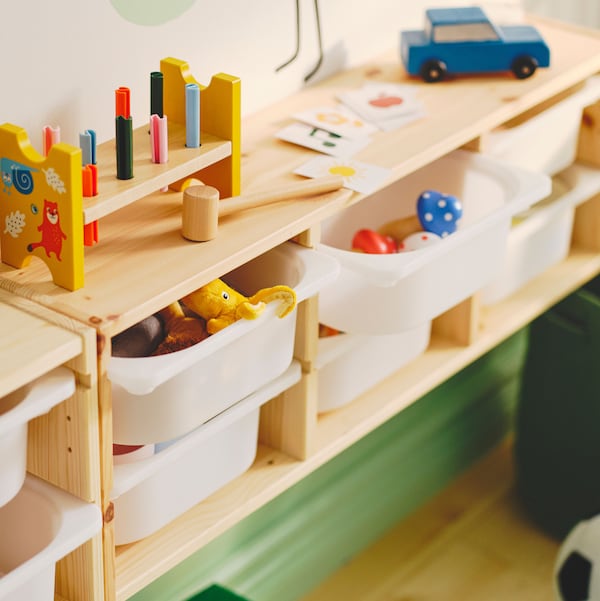 A light white stained pine TROFAST wall storage holding white storage boxes and with an UPPSTÅ toy hammering block on top.