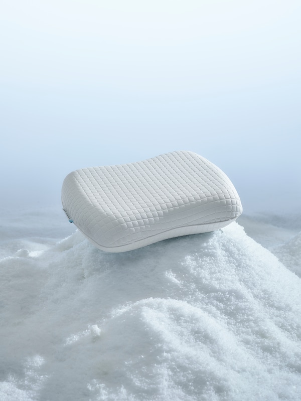 An ergonomic foam pillow with cooling gel is sitting on top of a pile of snow in a white space.