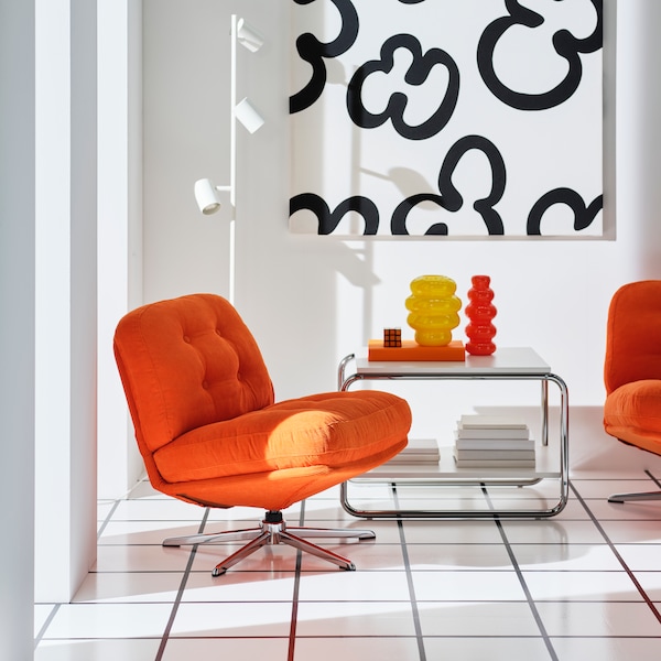 Two orange DYLINGE swivel armchairs are placed next to a coffee table with one yellow and one orange KÄLLARHALS vase on it.