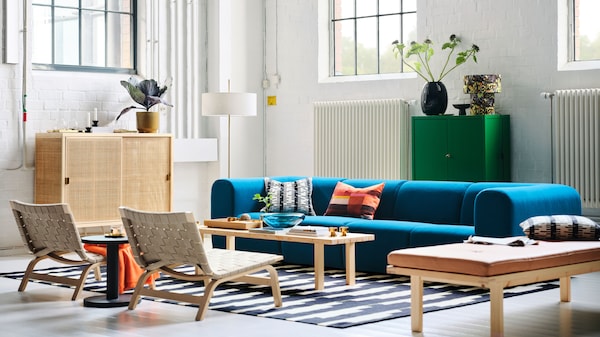 A living room with a dark turquoise STOCKHOLM 2025 4-seat sofa, easy chairs, and a floor lamp arranged around a coffee table.
