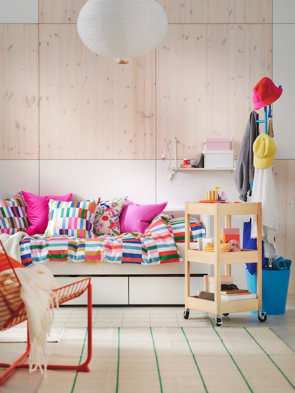 White and light wood 24-hour living space with white daybed with bright coloured checked bedding and pink cushions.

