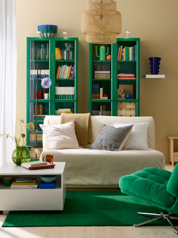 Living room with two green glass display cabinets side by side, small sofa-bed with beige cover and green rug.