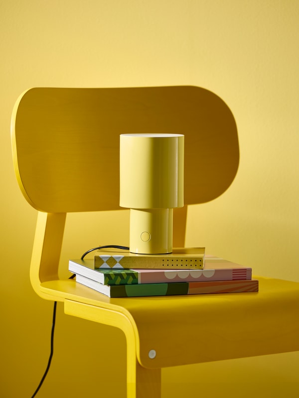 Close-up of a yellow table lamp and books on a yellow chair, in front of a yellow wall.