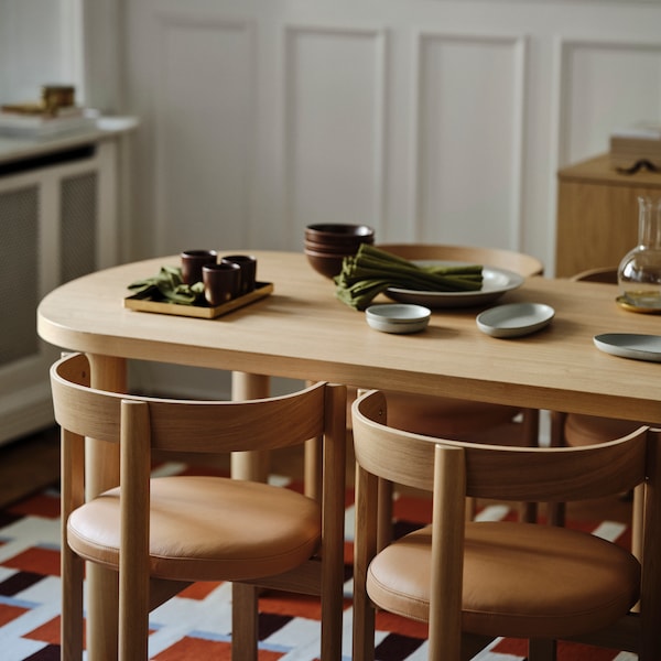 Four oak and leather STOCKHOLM 2025 chairs around an oak table with a carafe, bowls, napkins, and other items on it.