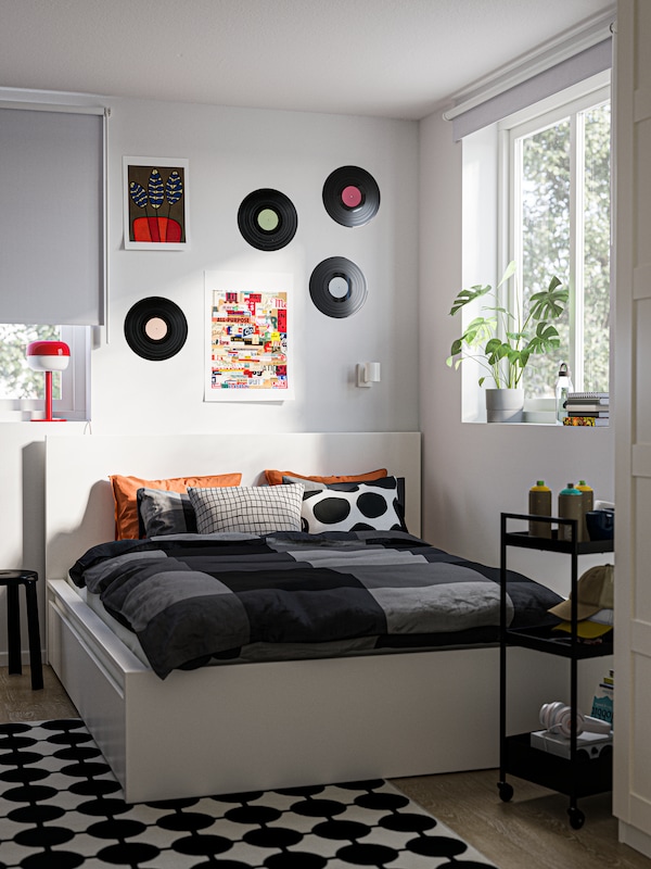 A corner of a bedroom with a MALM bed, a black/white VÄNDPLATS rug on the floor and old records on the wall above the bed.