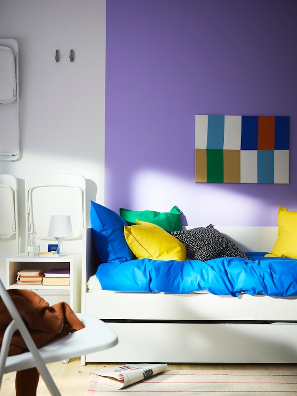 VIHALS day-bed in white, with trundle bed below and the wall behind it painted purple. Bright blue and yellow bedding.