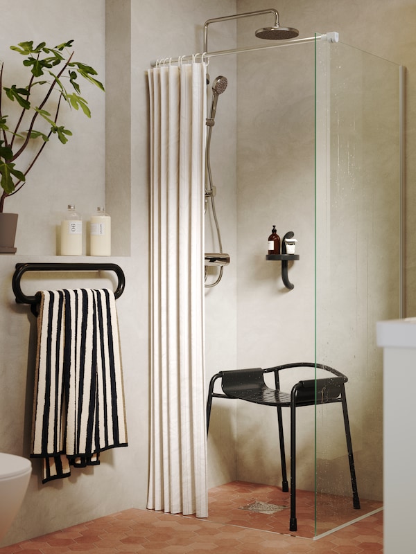 A softly beige bathroom has a BÄSINGEN shower chair, a BÄSINGEN towel rail and a BÄSINGEN shower shelf in anthracite.
