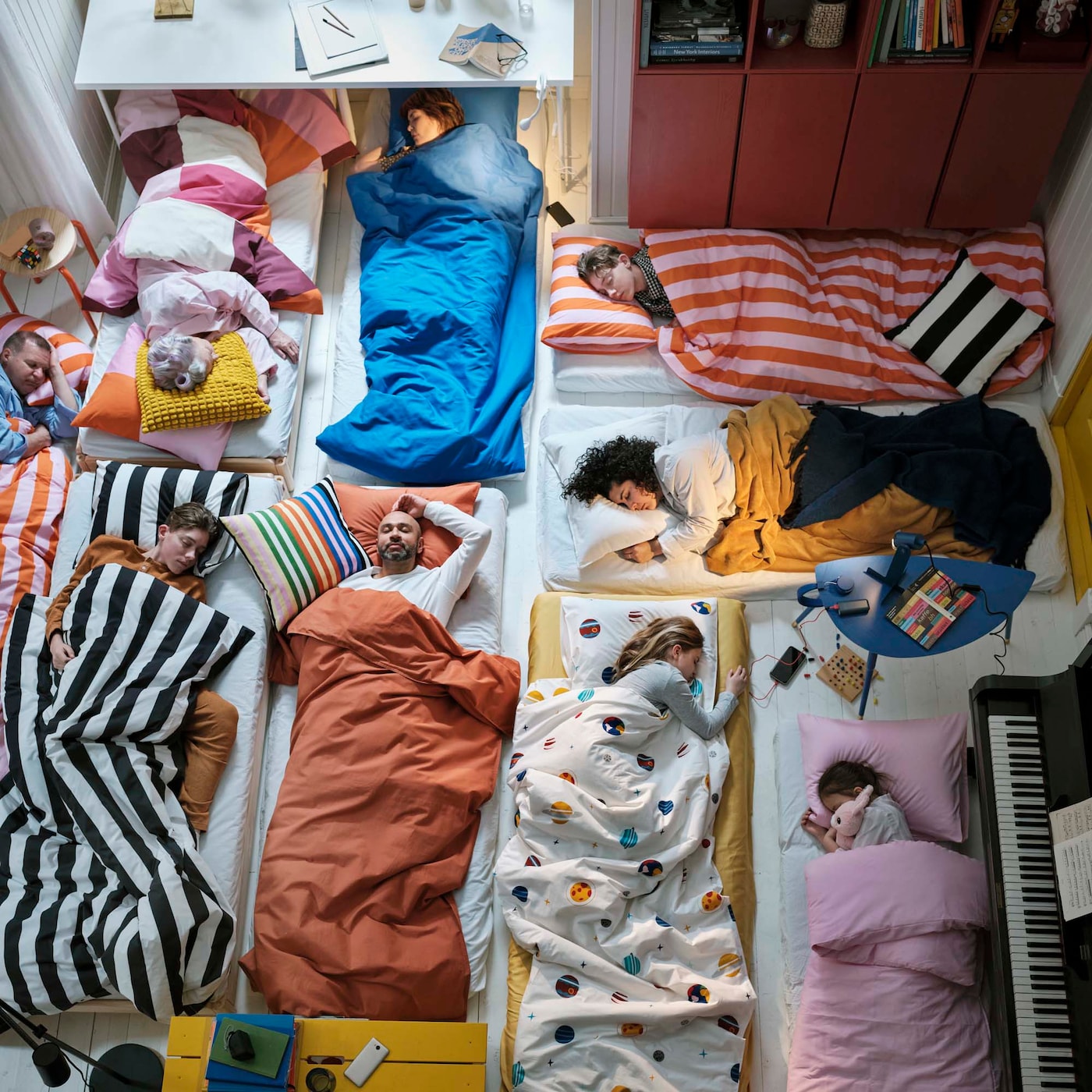 People sleeping on a white floor on single mattresses dressed in various colourful IKEA bedding.