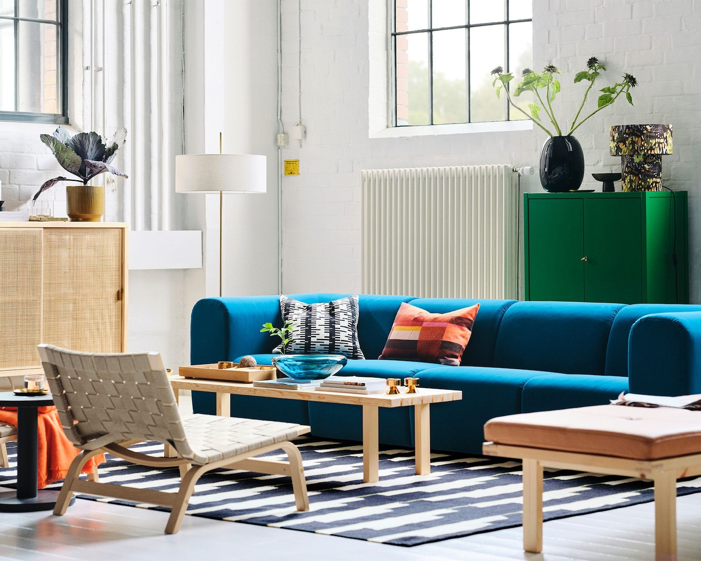 A white living room with tall windows, with a blue sofa and light wood furniture from the STOCKHOLM collection.